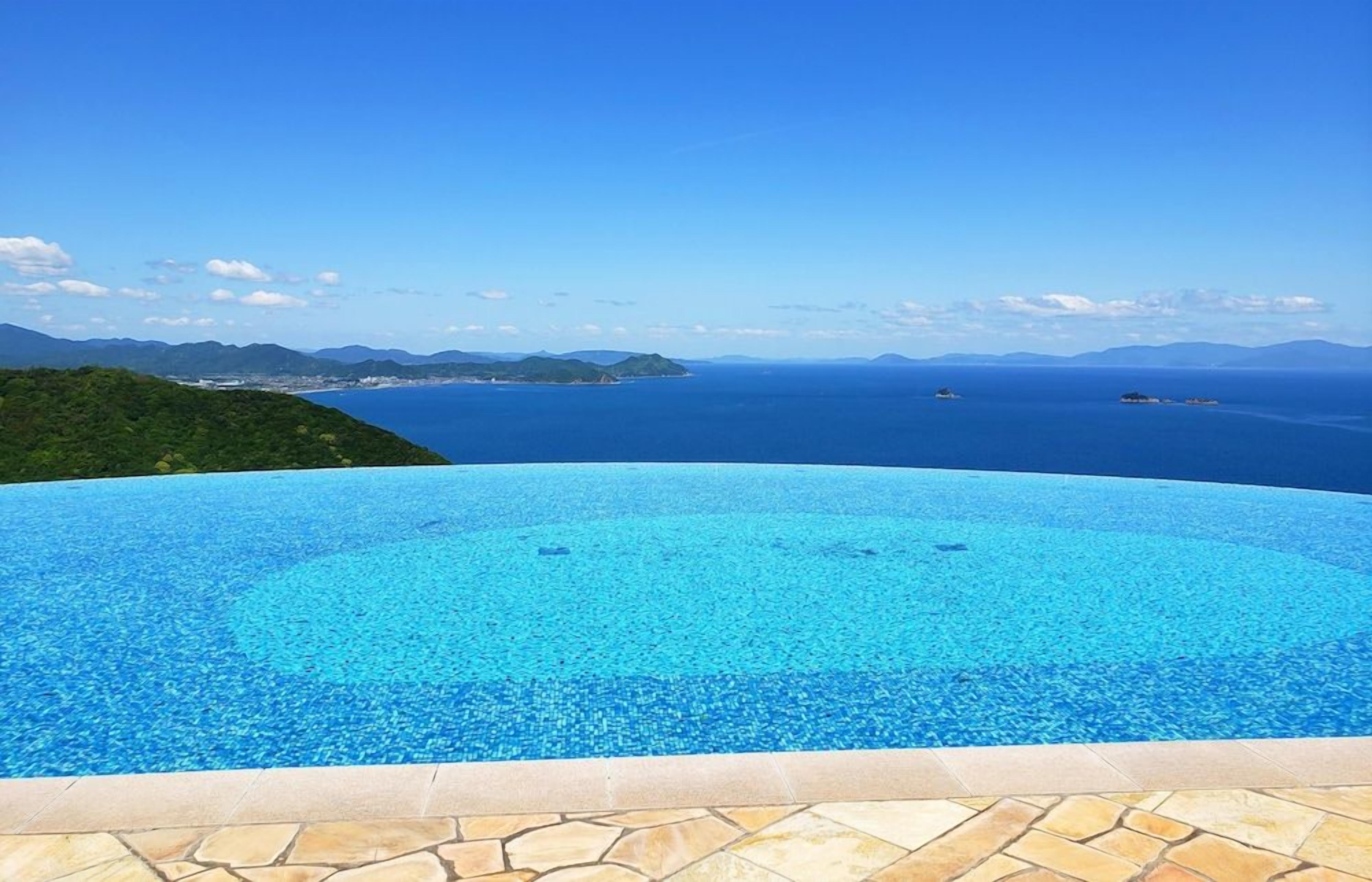 Una piscina infinita azul cristalina con vistas al océano y montañas a lo lejos.