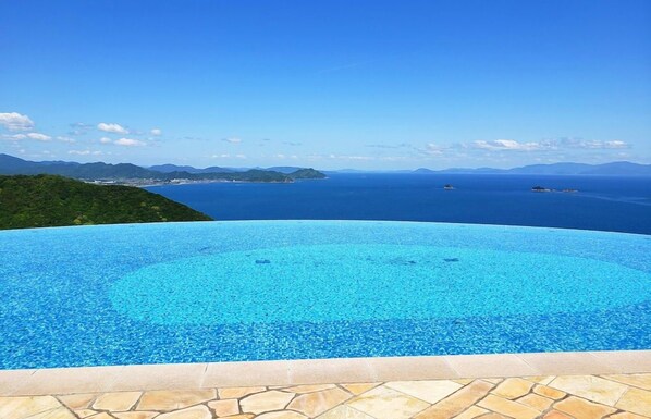 Una piscina infinita azul cristalina con vistas al océano y montañas a lo lejos.