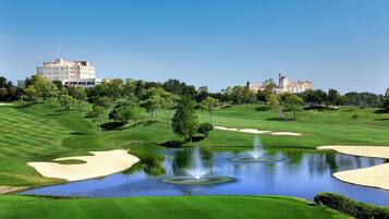 Un campo de golf con búnkeres, un estanque con fuentes y edificios al fondo.