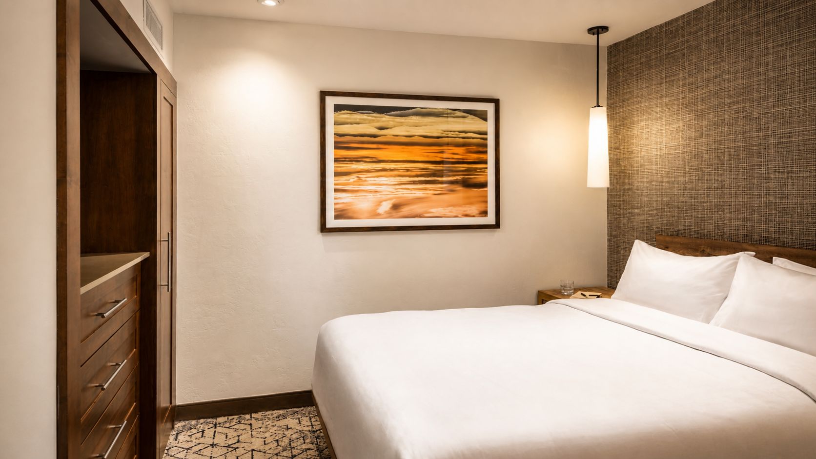 A hotel room with a bed, a nightstand, a framed picture on the wall, and a wardrobe.