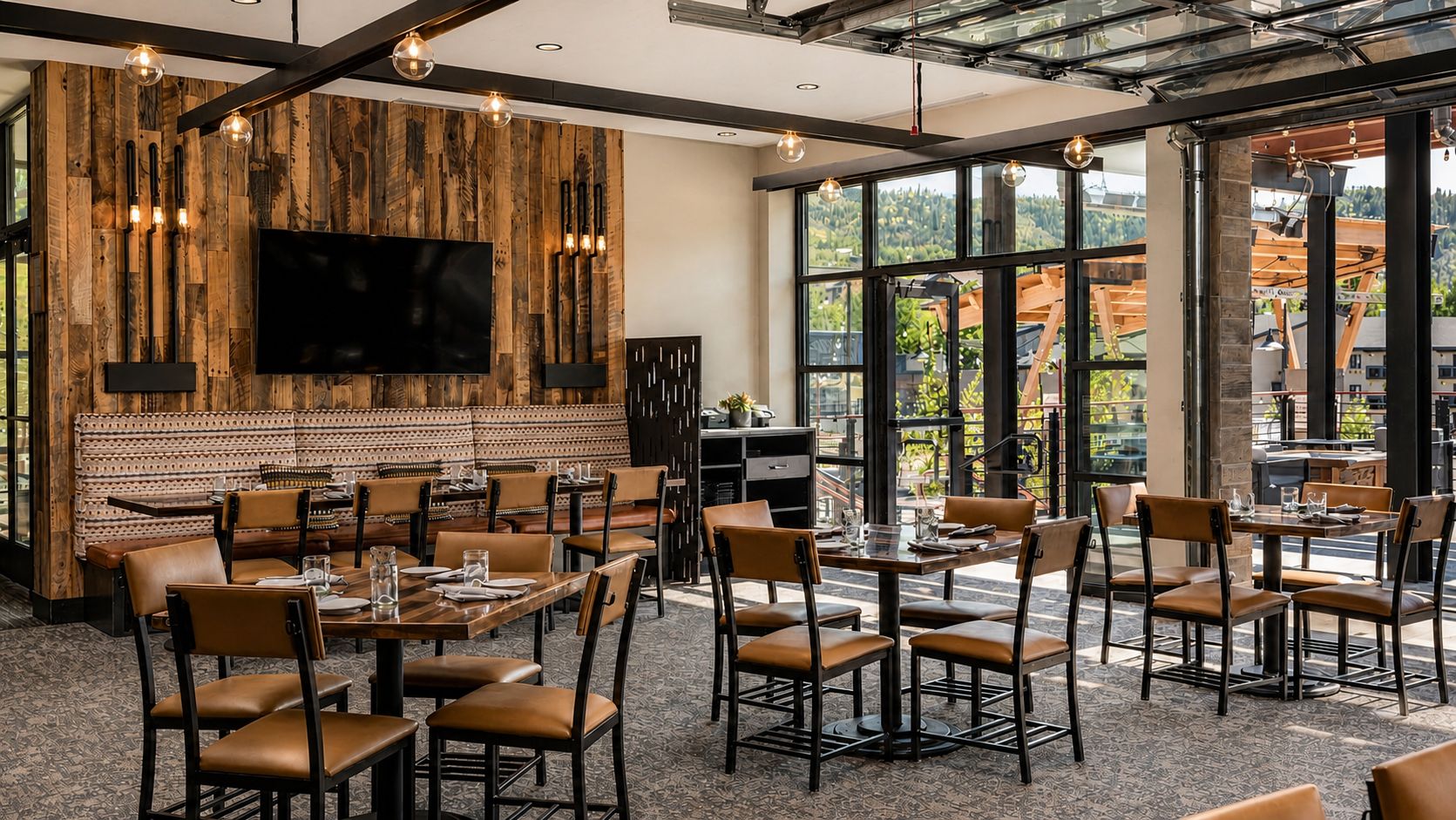 Un restaurant doté de nombreuses tables et chaises, d’un grand téléviseur à écran plat fixé à un mur en bois, et de grandes fenêtres offrant une vue sur l’extérieur.