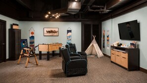 Una habitación con mesa de fútbol, sillones reclinables, una tienda de campaña y un televisor.