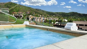 Une piscine avec vue sur une ville située sur une colline, un télésiège et un bâtiment portant l’inscription « Boat ».