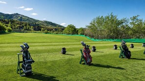 Golfkenttä, jossa on useita golfvälineitä sisältäviä laukkuja ja josta avautuu selkeä näkymä ympäröivään maisemaan.