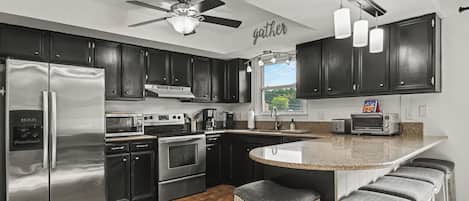 A modern kitchen with dark cabinets, stainless appliances, a central island with bar stools, and a ceiling fan.