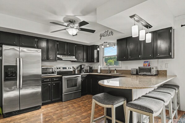 A modern kitchen with dark cabinets, stainless appliances, a central island with bar stools, and a ceiling fan.