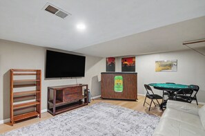 A room with a flat-screen TV, a wooden cabinet, a pool table, and a folding chair. - Notre Dame Game Day Getaway! Minutes from Campus, South Bend & Eddy Street (South Bend)