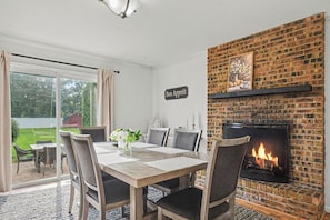 Comedor con chimenea de ladrillo, una mesa con sillas y vistas al exterior.