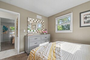 A bedroom with a bed, dresser, and a window with a view.