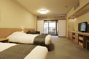 Habitación de hotel con dos camas, televisión, escritorio y puerta corrediza a un balcón.