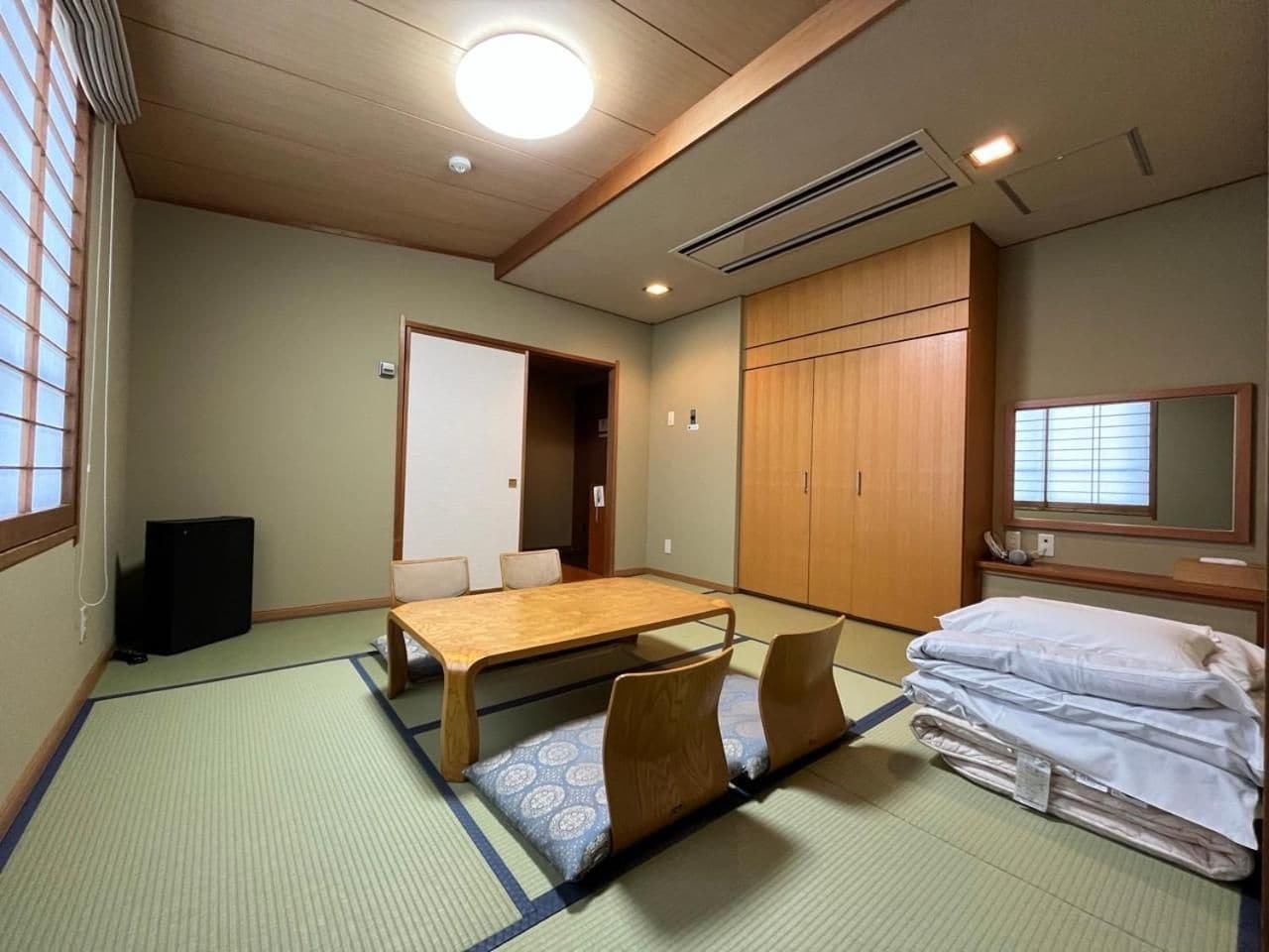 Habitació tradicional japonesa amb tatami, una taula baixa, un llit amb roba de llit blanca i un gran armari de fusta.