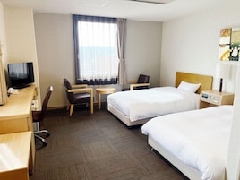 Habitación de hotel con dos camas, un escritorio con televisor, una silla, una mesita y una ventana con cortinas.