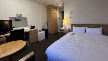 Habitación de hotel con cama, escritorio, silla, televisor y una kitchenette pequeña.