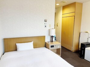 Een hotelkamer met een bed, nachtkastje, lamp en een kledingkast.