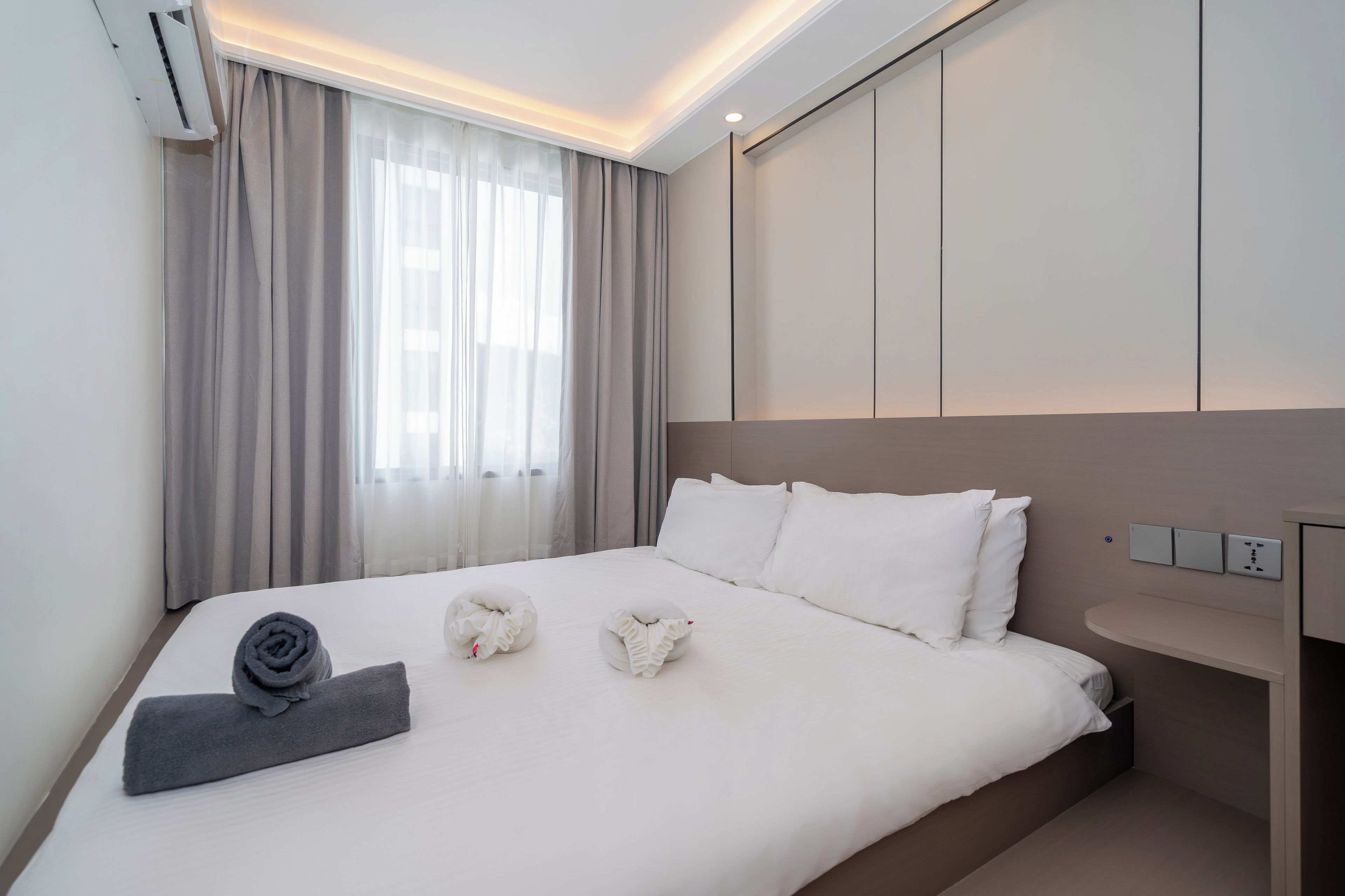 Une chambre d’hôtel avec un lit, une table de chevet, un climatiseur fixé au mur et une fenêtre avec des rideaux.