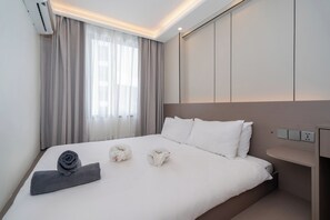 Una habitació d'hotel amb un llit, una taula de nit, un aire condicionat fixat a la paret i una finestra amb cortines.