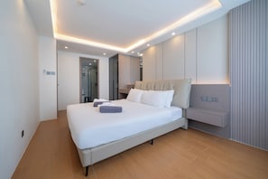 A modern hotel room with a large bed, a bedside table, a built-in wardrobe, and a shower area. - Modern 2BR Apt near Bangtao Beach - Pool - Gym & WiFi (Choeng Thale)