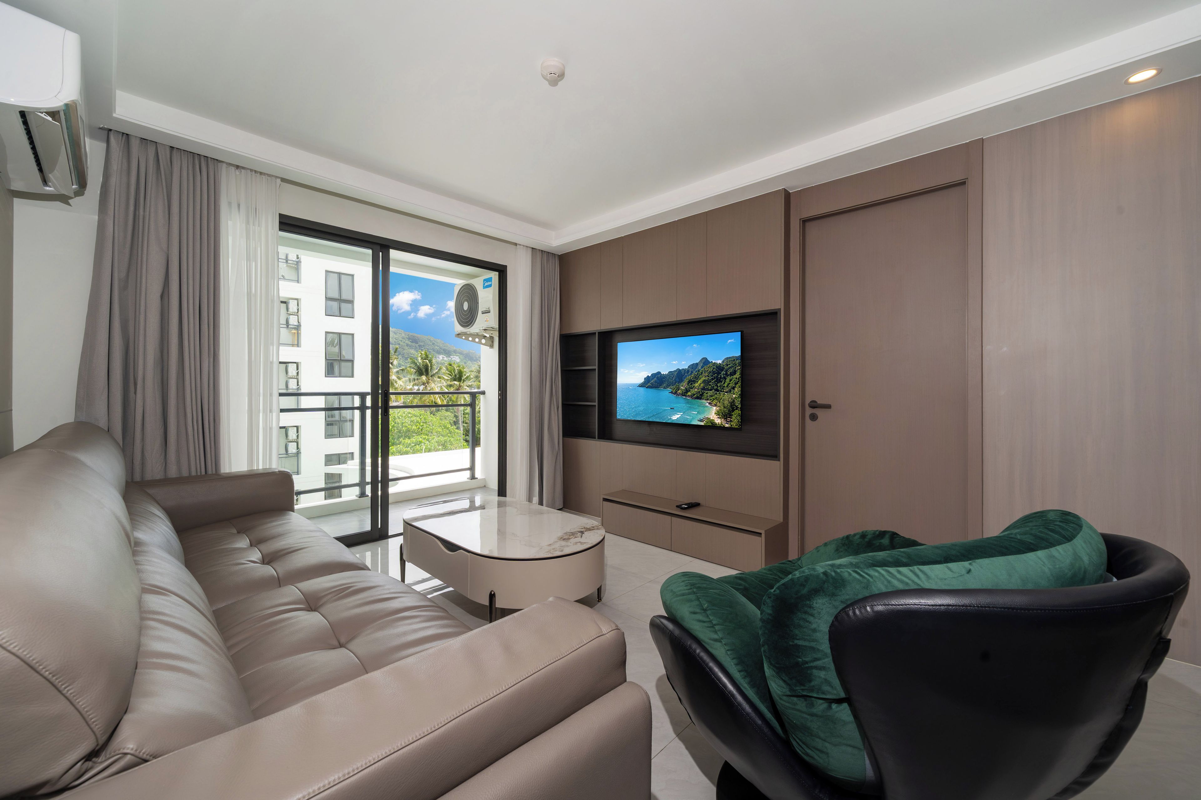 Une chambre d’hôtel moderne équipée d’un canapé, d’un téléviseur fixé au mur, d’un balcon offrant une vue sur les bâtiments et la verdure, et d’un climatiseur installé au plafond.