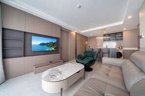 A modern living room with a flat-screen TV, a marble coffee table, a green chair, and a beige sofa. - Modern 2BR Apt near Bangtao Beach - Pool - Gym & WiFi (Choeng Thale)