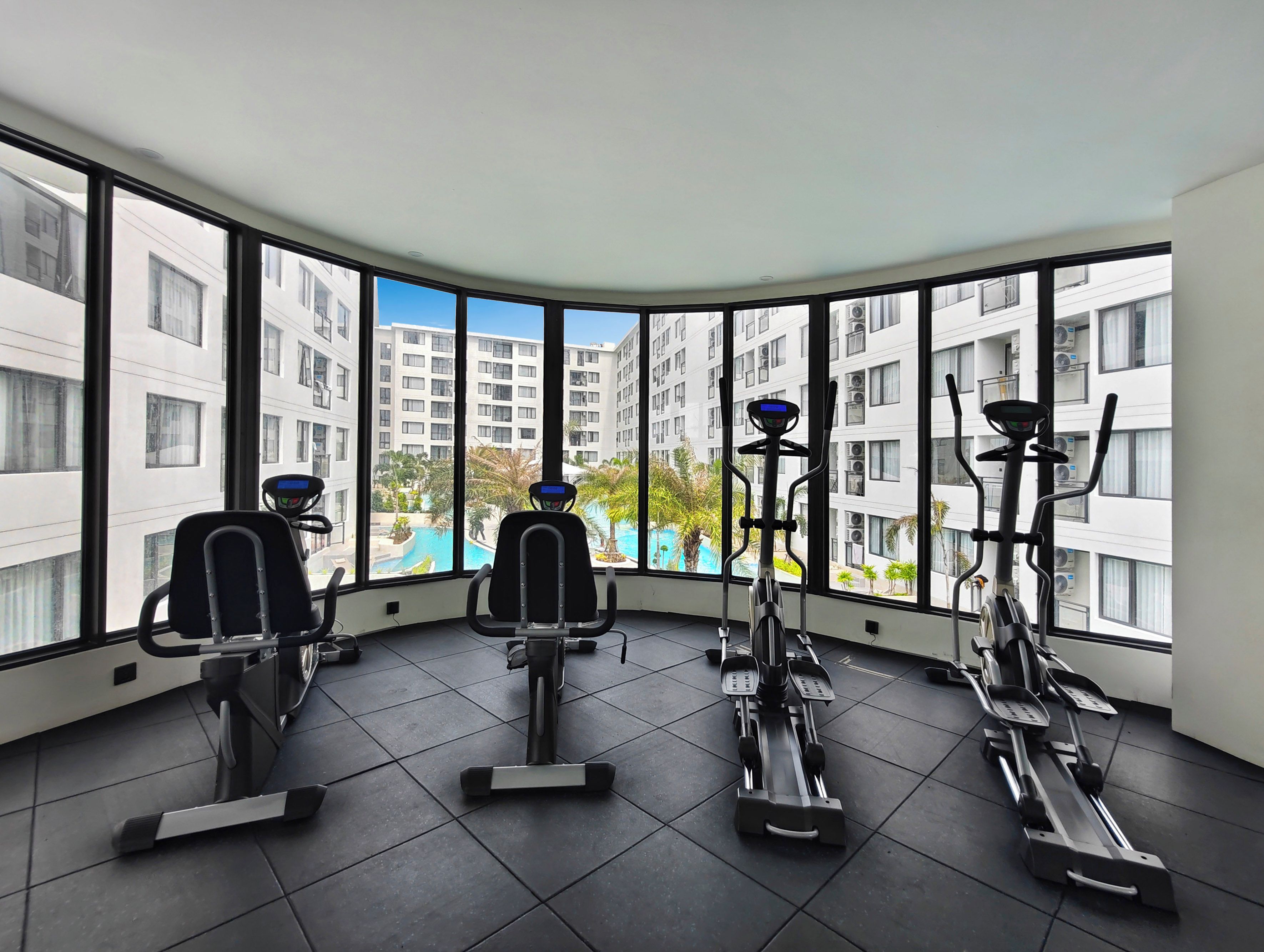 Une salle de sport équipée de matériel d’exercice et dotée de grandes fenêtres donnant sur un quartier résidentiel.