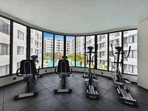Un gimnasio con equipamiento de ejercicio y amplios ventanales con vistas a una zona residencial.