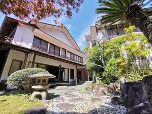 A traditional Japanese building with a covered walkway, stone lanterns, and a garden with rocks and plants. - Gyokushoen Arai (Izu)