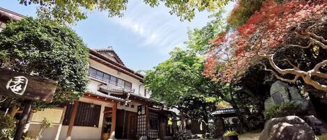Edificio japonés tradicional con una puerta de madera, rodeado de abundante vegetación y rocas.