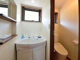 Un baño con un lavamanos blanco, una ventana encima y un inodoro.