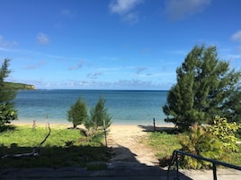 Una playa con agua cristalina, un sendero arenoso y vegetación.