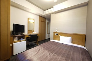Habitación de hotel con cama, escritorio, computadora, televisión y refrigerador pequeño.