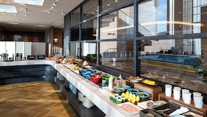 A buffet area with a variety of food items and beverages, a long counter, and a view of the kitchen through large windows. - Hotel City Plaza Kitakami (Kitakami)