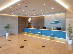 Un espace d’accueil moderne avec un comptoir bleu, deux tabourets de bar et une plante en pot.