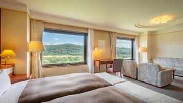 Habitación de hotel con dos camas, un escritorio, un sofá y ventanas amplias con vista a zonas verdes.