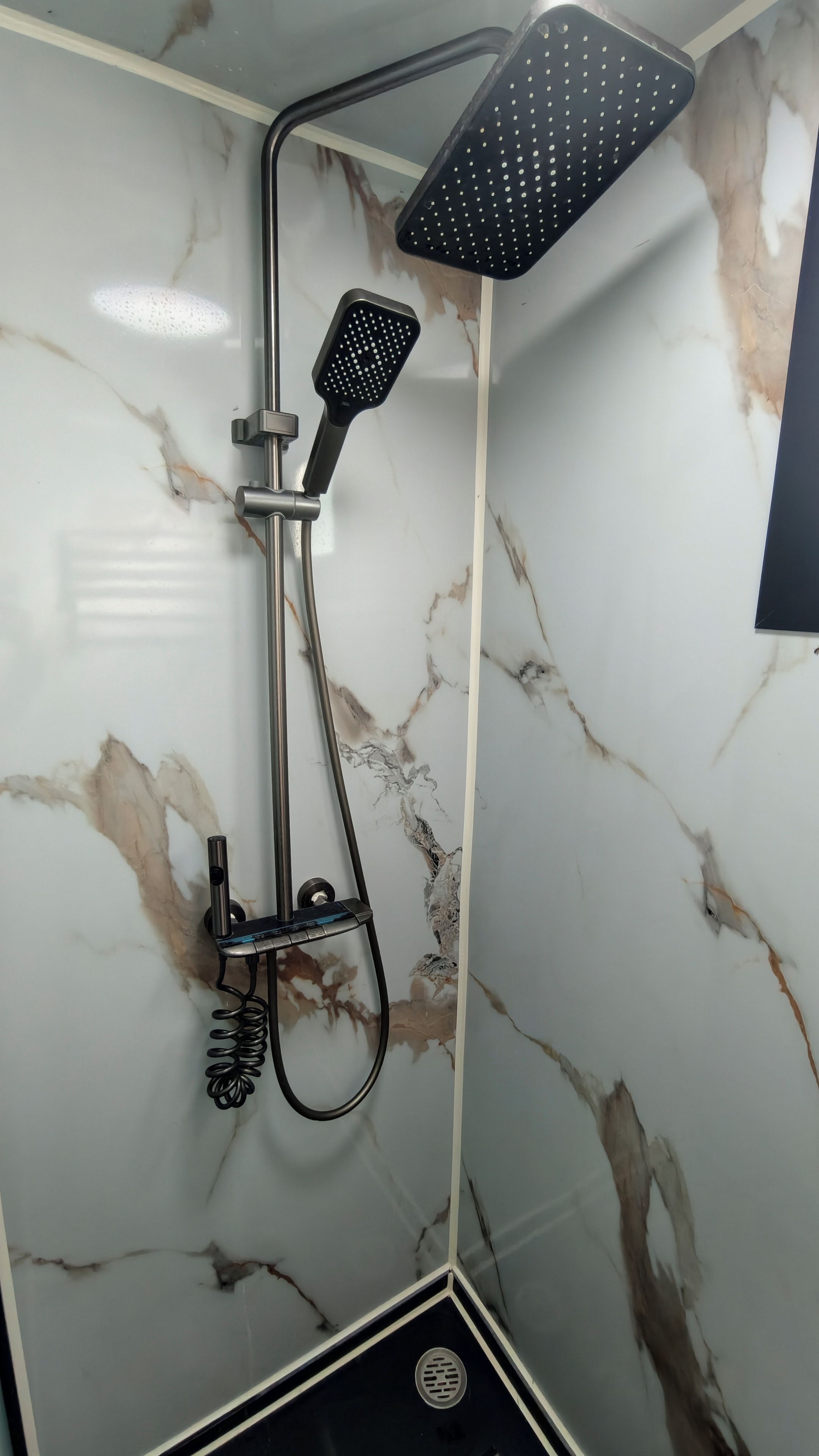 Ducha con cabezal de ducha manual y cabezal de ducha fijo, ambos instalados en una pared con estampado tipo mármol.