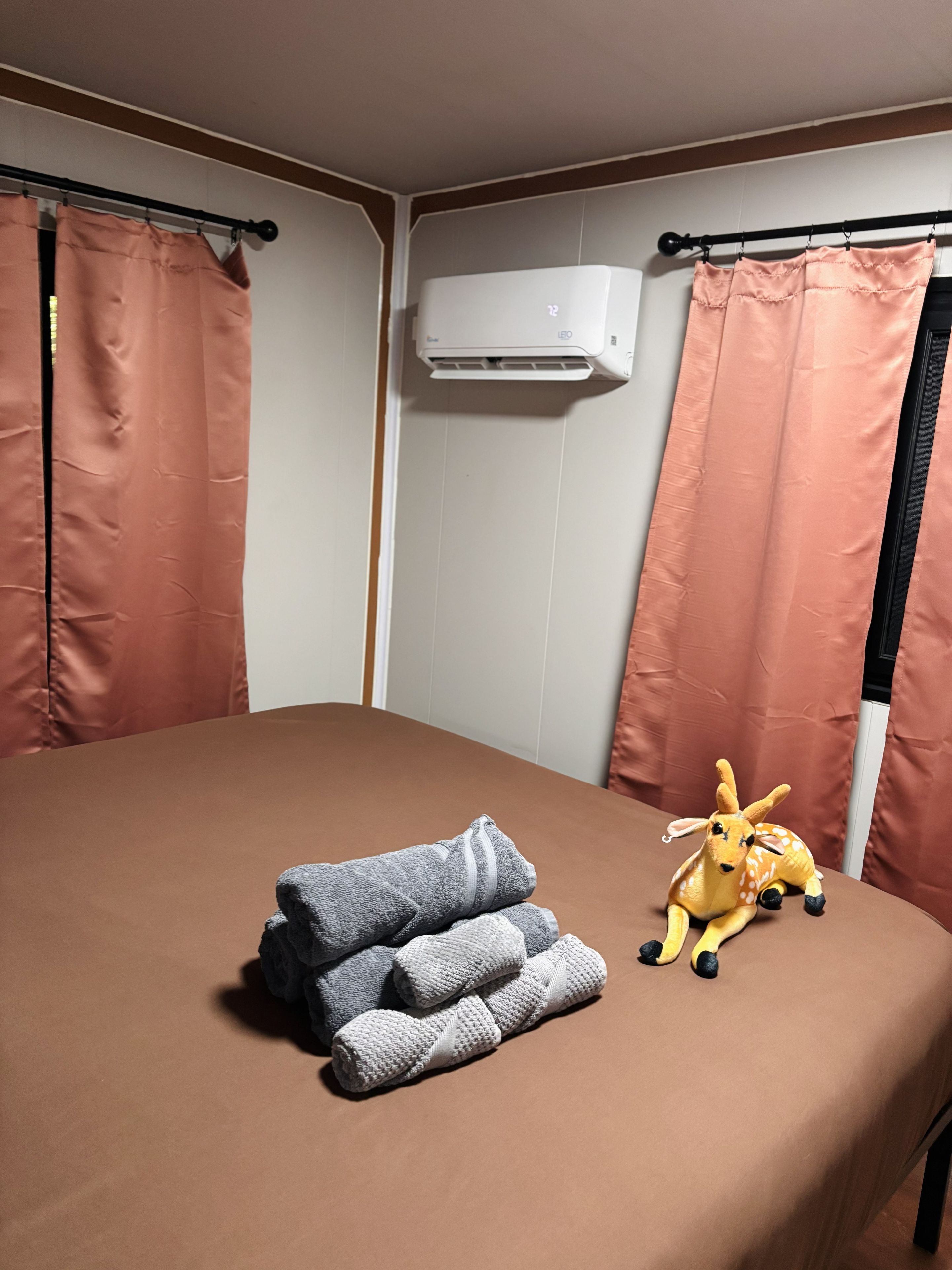 Una habitación con una cama, aire acondicionado de pared y un peluche sobre la cama.