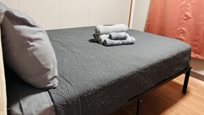 Ein Einzelbett mit grau strukturierter Matratze, einem grauen Kopfkissen und darauf gerollten Handtüchern.