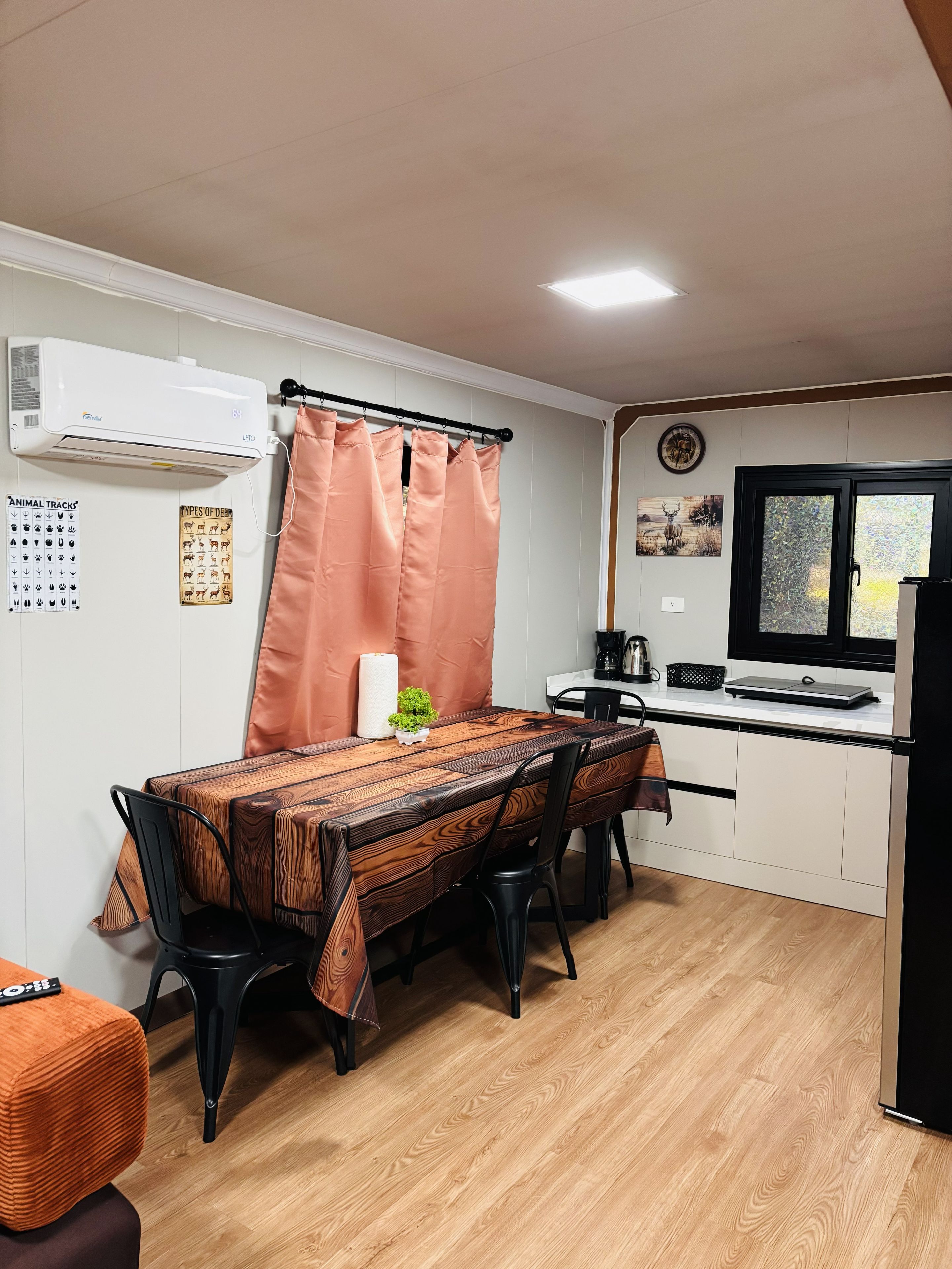 Een gezellige keuken met eethoek, met een houten tafel, stoelen, een klein plantje en een koelkast.