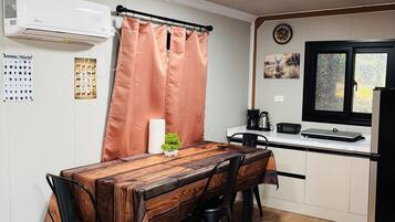 Een gezellige keuken met eethoek, met een houten tafel, stoelen, een klein plantje en een koelkast.