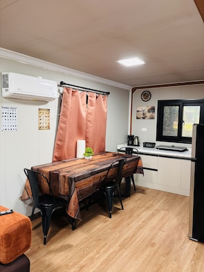 Cocina compacta con comedor, que incluye una mesa de madera, sillas, una planta pequeña y un refrigerador.