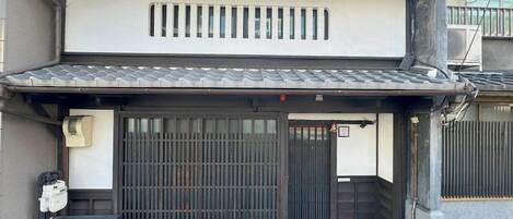 A traditional Japanese building with a sliding gate, a small air conditioning unit, and a tiled roof.