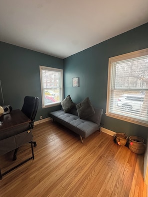 Ein Zimmer mit einer dunkel-türkisfarbenen Wand, einem grauen Sofa, einem Holztisch und einem Fenster mit Jalousien.