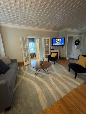 Ein Wohnzimmer mit Sofa, Sessel, Couchtisch und einem an der Wand befestigten Fernseher.