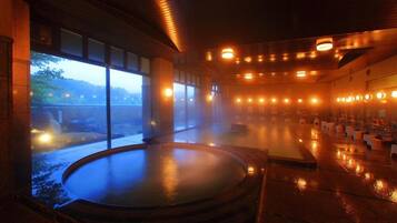 A hot spring bath area with a view of the outdoors, a wooden ceiling, and a series of lights.