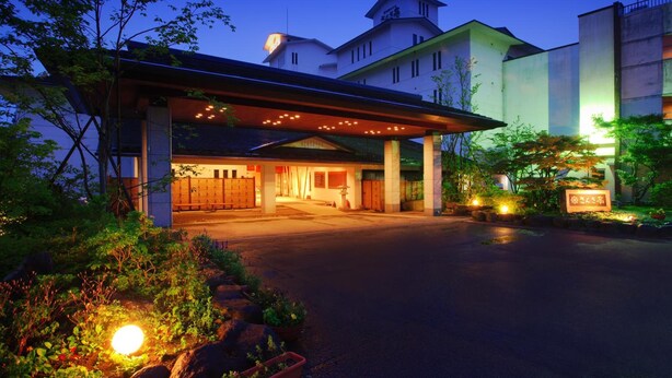 Entrada de um hotel com galeria coberta, área de estacionamento e placa.