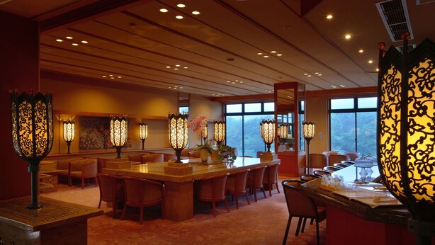 A hotel dining area with a long bar, multiple tables, and decorative lighting fixtures.