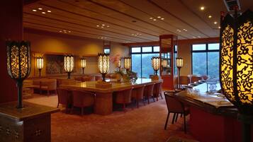 A hotel dining area with a long bar, multiple tables, and decorative lighting fixtures.