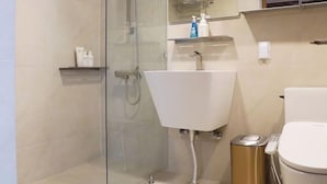 A modern bathroom with a glass-enclosed shower, a white sink, and a toilet.