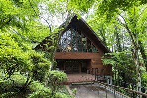 A wooden cabin with a steep roof, surrounded by dense green foliage. - Seimei No Mori Resorts (Chiba)