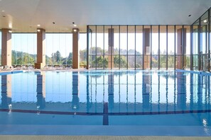 Une piscine intérieure avec des parois en verre transparent, un sol carrelé et une vue sur le paysage environnant.