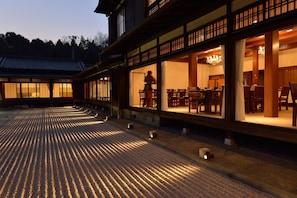 Un bâtiment traditionnel japonais doté d’un espace extérieur couvert avec des sièges et d’une salle à manger visible à travers les fenêtres.
